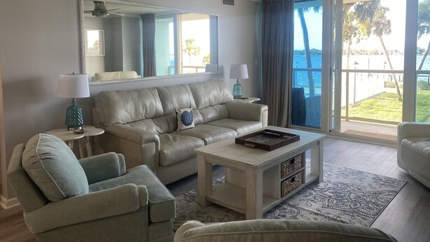 Una sala de estar con un sofá de cuero color beige, un sillón gris, una mesa de centro y un ventanal con vista al océano.