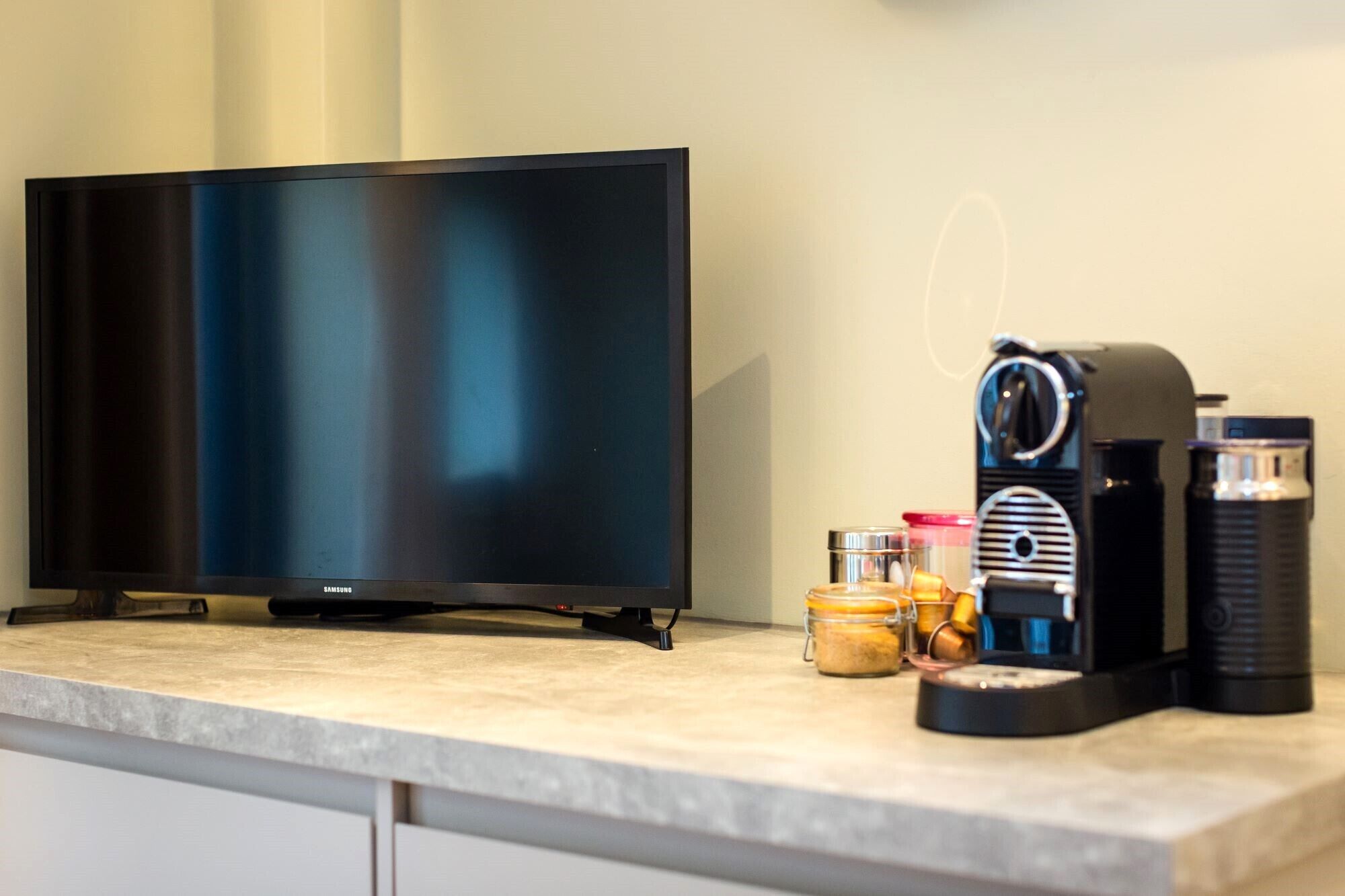Una encimera de cocina con un televisor de pantalla plana, una cafetera y frascos de especias.
