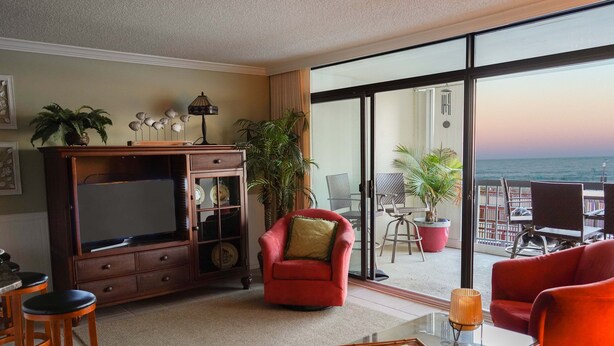 Une chambre d’hôtel avec un balcon, une télévision, un fauteuil rouge et une table basse en verre.