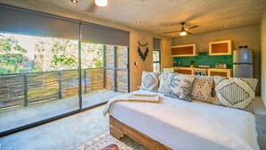 A bedroom with a large bed, a ceiling fan, a view through a sliding door, and a kitchenette with a refrigerator and stove. - Eco-sustainable Luxury Between Beach Hotspots & Tulum Town by Stella Rentals (Tulum)