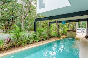 Una piscina con caída de agua, rodeada de abundante vegetación y árboles.
