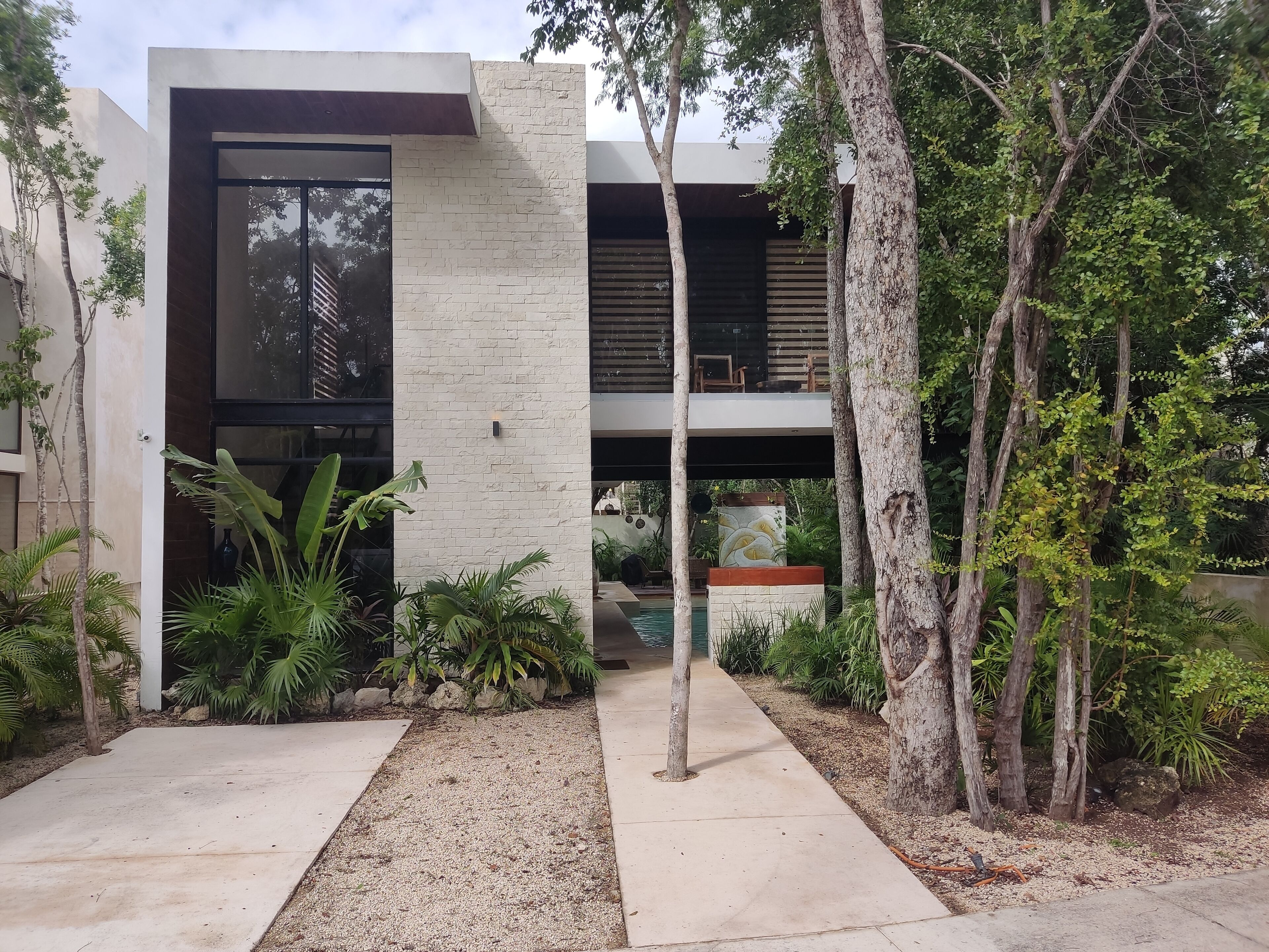 Un edificio moderno con fachada de hormigón, amplias ventanas y un jardín con árboles y plantas.