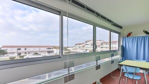 En balkon med bord og stole, store vinduer med udsigt til bygninger, og et gardin.