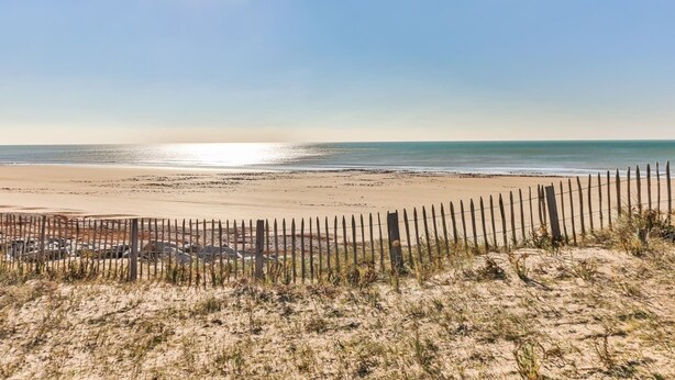 En strand med et træhegn i forgrunden, sand og en klar himmel.