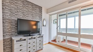 Et værelse med stenvæg, et fladskærms-tv på et skab, en skydedør til en balkon, og et lille hvidt skab.