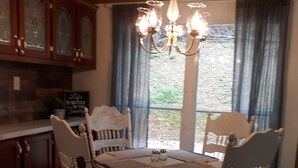 Spiseområde med et rundt bord, fire stole, en lysekrone og udsigt gennem et vindue med gardiner.