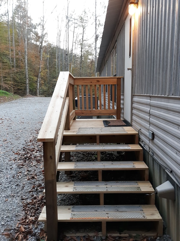 A wooden staircase leading to a deck with metal safety grates, a metal wall, and a forested background.
