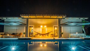 Un área moderna junto a la piscina con una hamaca, asientos y un interior bien iluminado.