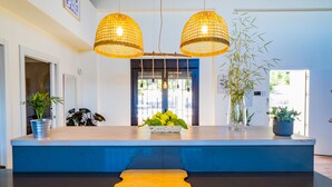 Un área de recepción con mostrador de madera, dos lámparas colgantes de mimbre y plantas en macetas.