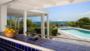 Zona junto a la piscina con vistas al océano, un espacio de descanso cubierto y un frutero sobre una encimera de baldosas.