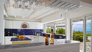 Una cocina moderna con una isla grande, salpicadero de azulejos azules y vista al océano.