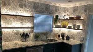 A kitchen with a patterned backsplash, a built-in dishwasher, and a window with blinds. - Stylish - Minutes From Beach, Bars & Eateries (West Palm Beach)