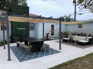 Uma área de pátio com mesa de jantar coberta, um sofá e um espaço de estar pequeno.
