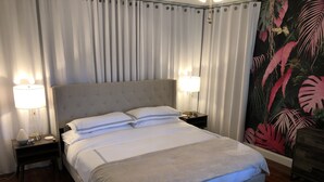 A hotel room with a large bed, two bedside tables with lamps, a nightstand, and a tropical-themed wall mural. - Stylish - Minutes From Beach, Bars & Eateries (West Palm Beach)