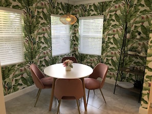 Uma área de refeições com uma mesa redonda, quatro cadeiras e um vaso de flores.
