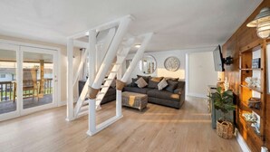 Een ruime woonkamer met een houten trap, een grijze bank en een groot raam.