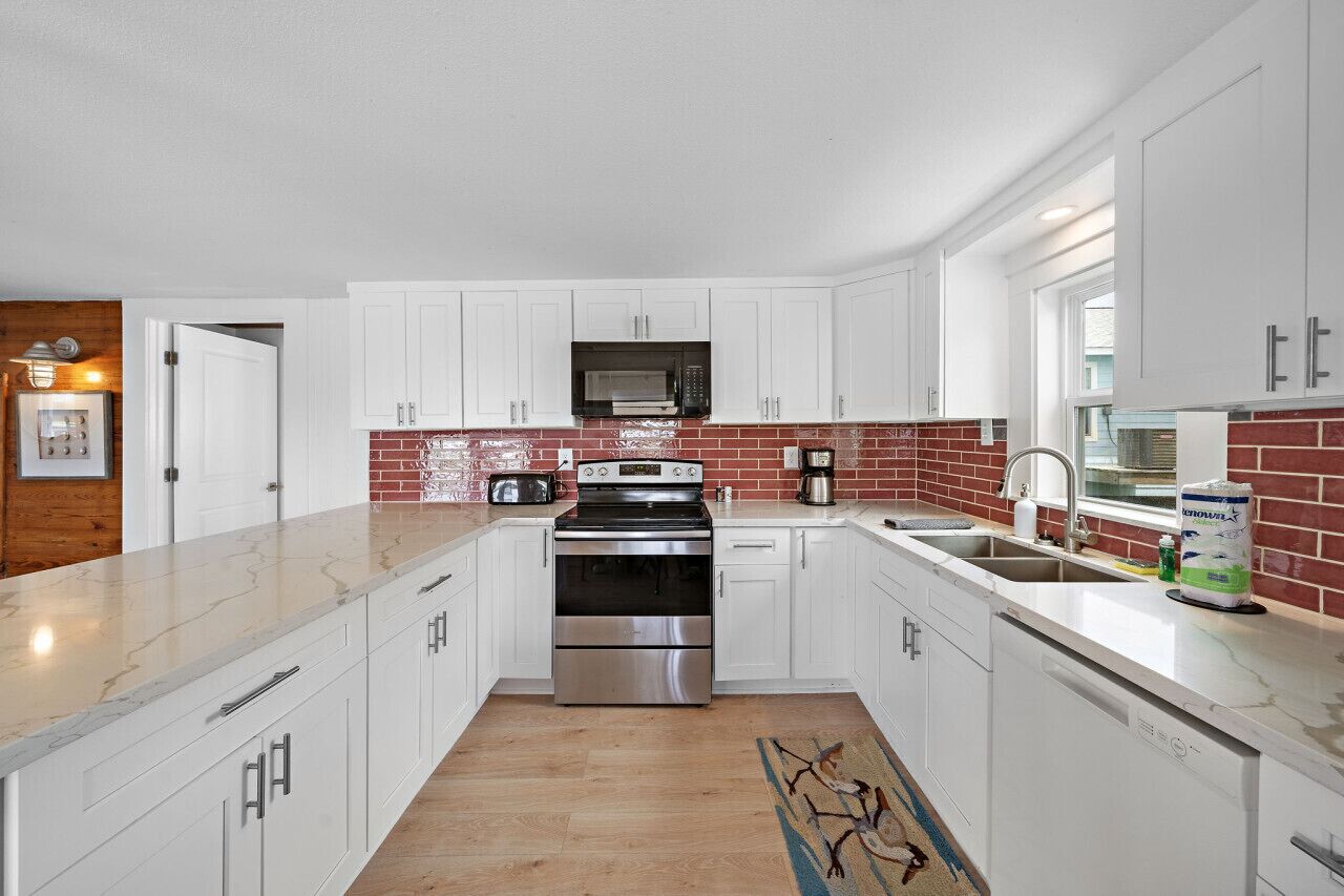 A modern kitchen with white cabinets, a stainless steel stove, a microwave, and a brick backsplash.