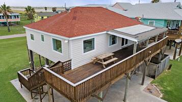 Une maison à deux étages avec un toit rouge, une terrasse en bois et des fondations en béton.