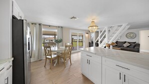 Een moderne keuken met witte kasten, een eethoek met houten stoelen, en een trap naar een balkon.