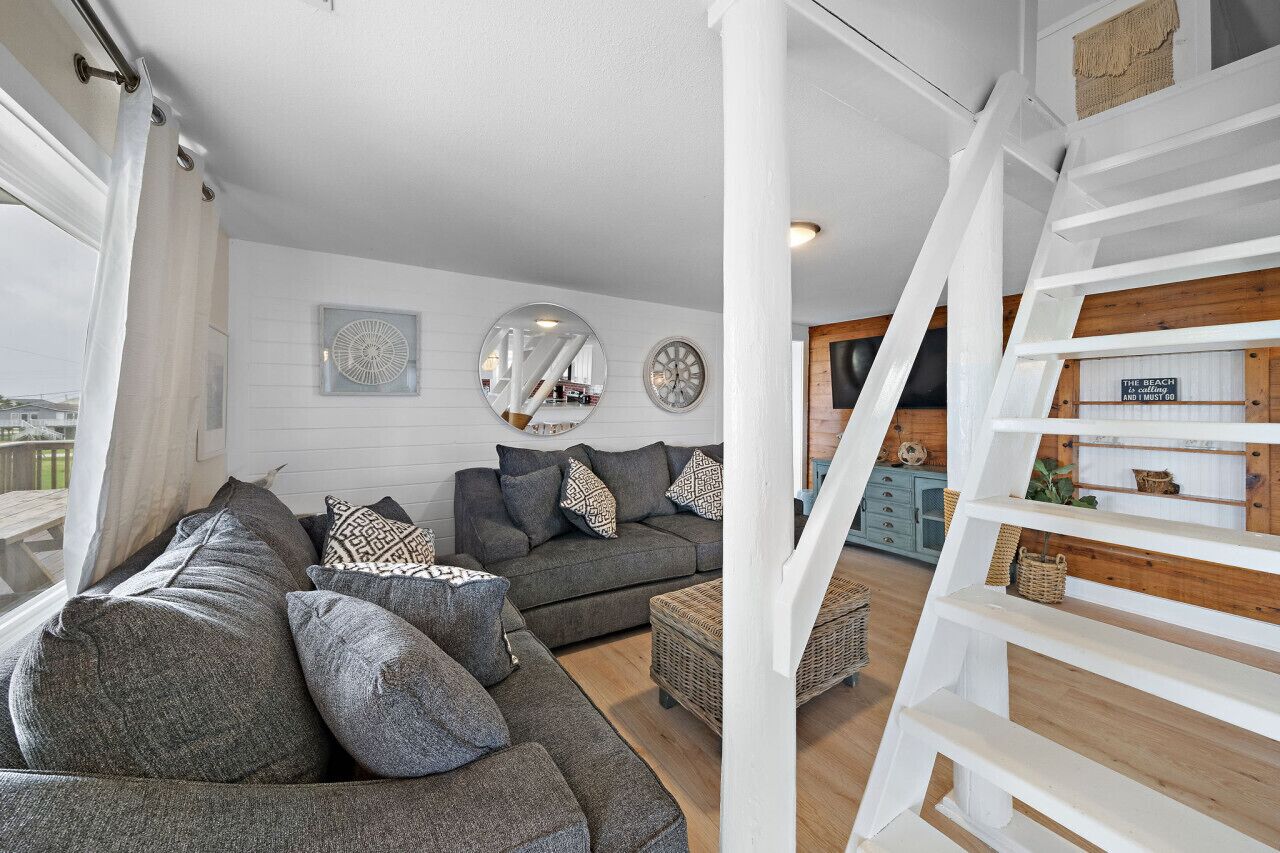 Una sala de estar moderna con un sofá seccional gris, una mesita de centro pequeña y una escalera con acabado de madera.