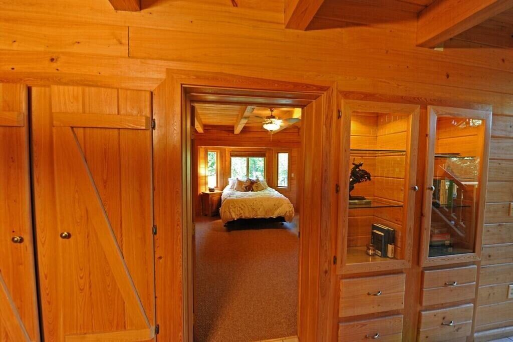 A wooden interior with a bed in the center, a staircase, and a glass cabinet.