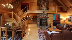 A spacious wooden cabin with a stone fireplace, a dining area, and a cozy living room with a couch and a fireplace. - Montana Mountain Log-Lodge with lake views, lake access & mountain views (Bigfork)