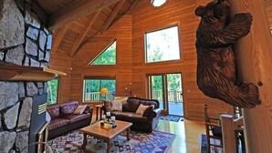 A spacious cabin interior with a stone wall, wooden beams, a bear sculpture, and large windows. - Montana Mountain Log-Lodge with lake views, lake access & mountain views (Bigfork)