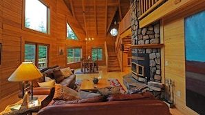 A log cabin interior with a stone fireplace, wooden floors, and large windows. - Montana Mountain Log-Lodge with lake views, lake access & mountain views (Bigfork)
