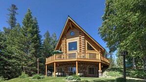 A log cabin with a stone foundation, a wooden deck, and a large window. - Montana Mountain Log-Lodge with lake views, lake access & mountain views (Bigfork)