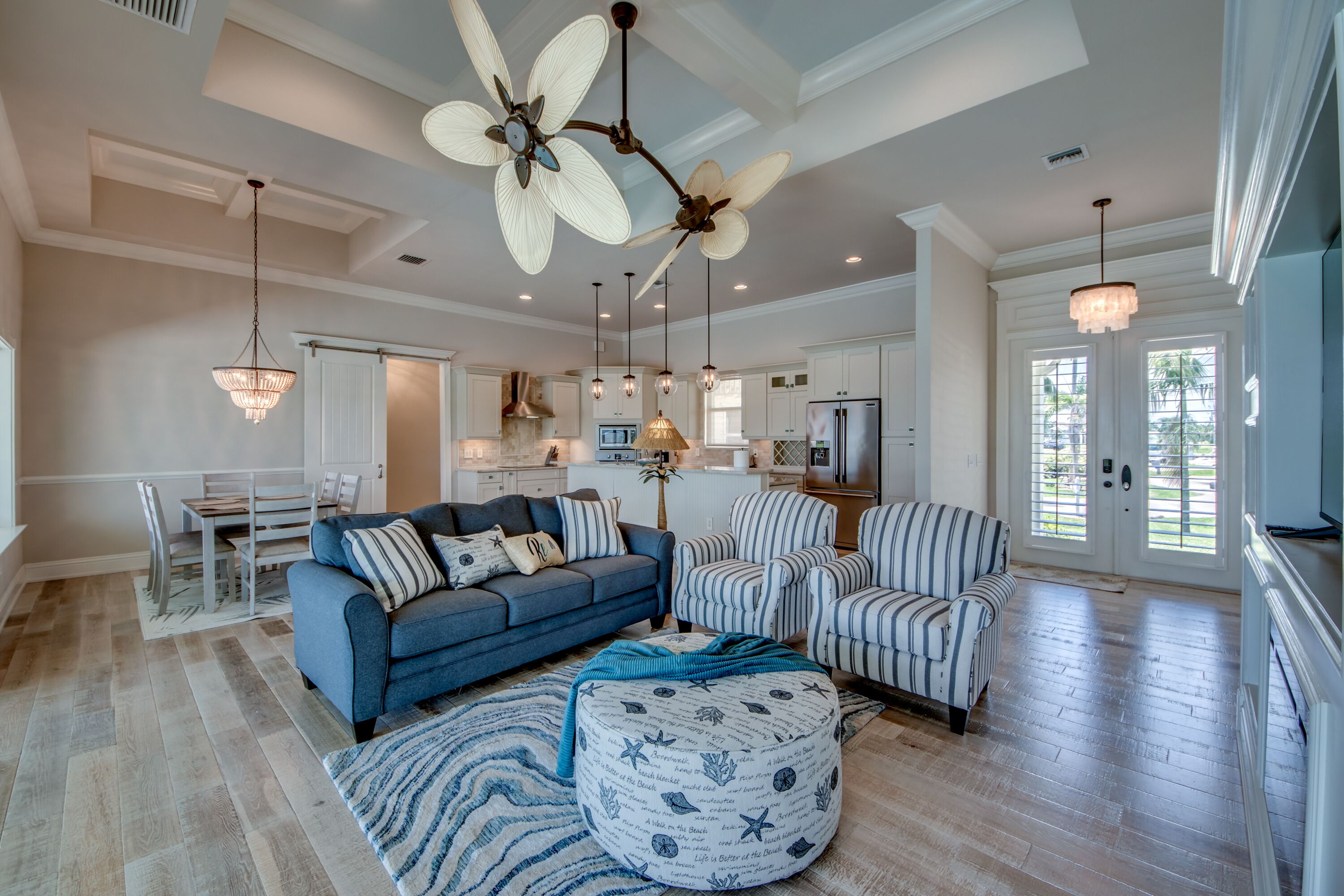 A spacious living room with a blue sofa, striped armchairs, and a round ottoman with nautical patterns.