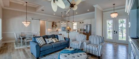 A spacious living room with a blue sofa, striped armchairs, and a round ottoman with nautical patterns.