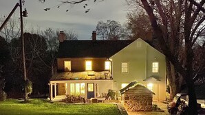 A two-story house with a well-lit porch and a stone structure in front.