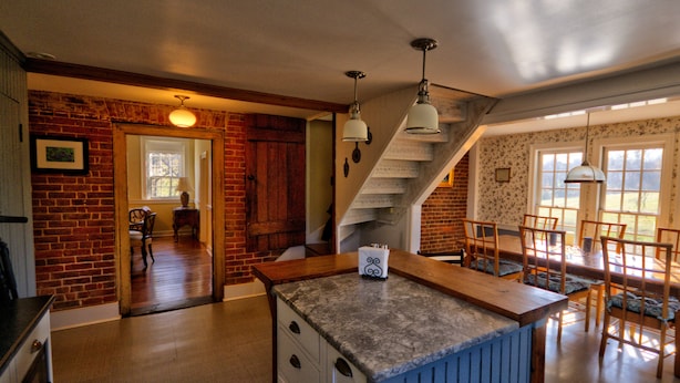 A kitchen with a marble countertop, wooden cabinets, and a dining area with a table and chairs.