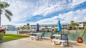 A waterfront patio with outdoor seating, a pool, and buildings in the background.