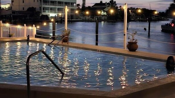 A pool area with a view of a building and a fence in the background.