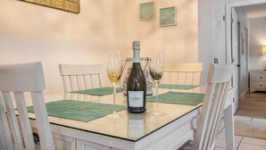 A dining table with a bottle of wine, two glasses, and green placemats.