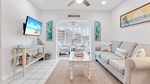 A living room with a ceiling fan, a flat-screen TV, a sofa, a coffee table, and a window with shutters.