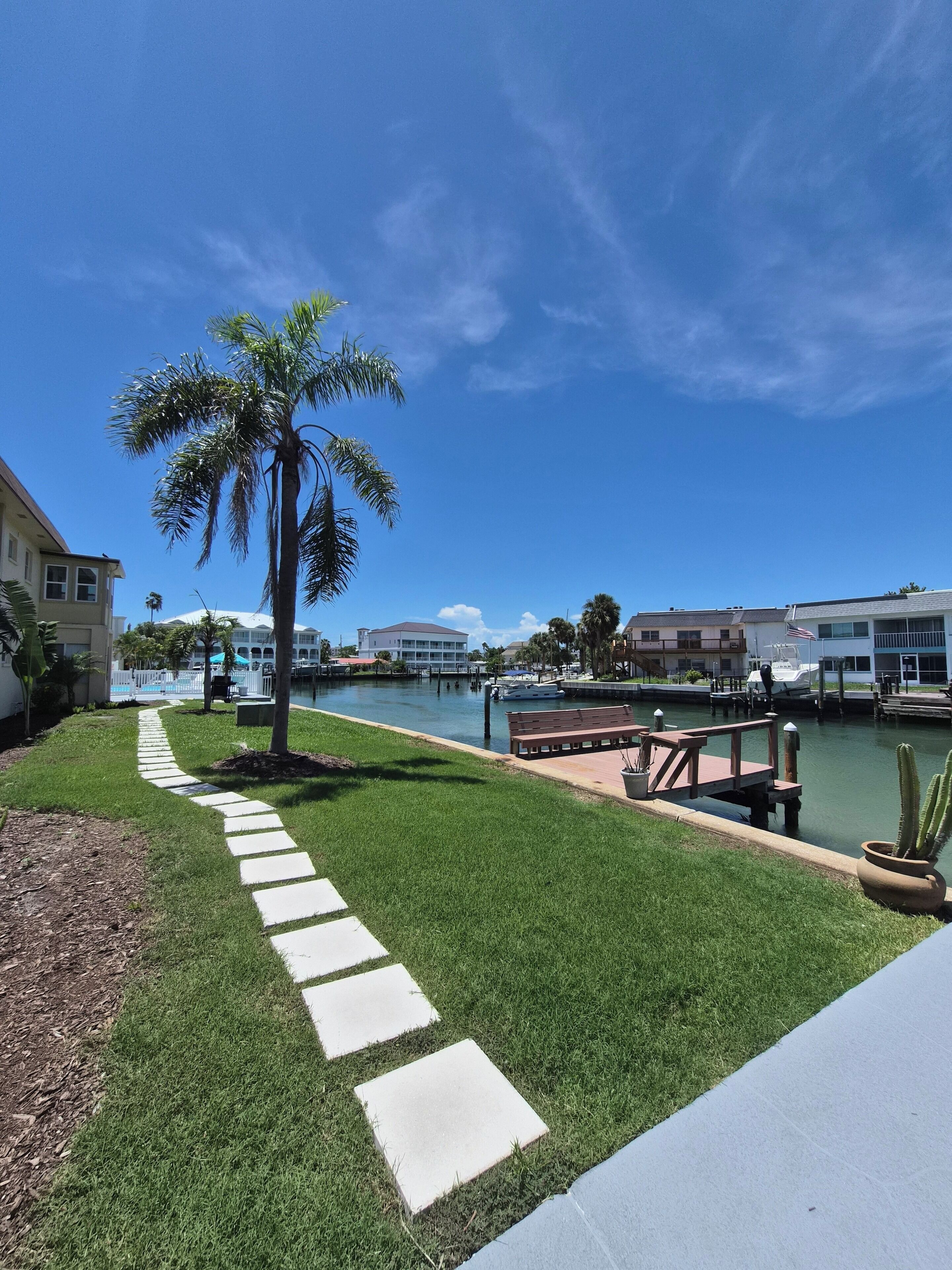 A waterfront property with a paved walkway, a palm tree, and a marina with boats.