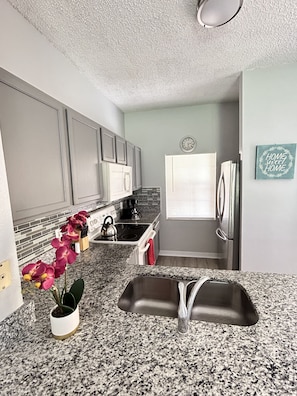 Una cocina moderna con encimeras de granito, un lavamanos de acero inoxidable y un horno empotrado.