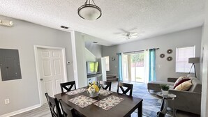 Un salon moderne avec un coin repas, comprenant une table en bois foncé, des chaises assorties et un ventilateur de plafond.