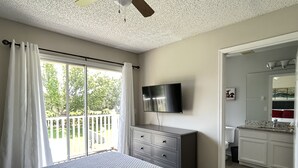 Une chambre à coucher comprenant un lit, un téléviseur fixé au mur, une commode et une porte-fen être coulissante donnant sur un balcon.