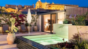 Eine Dachterrasse mit Whirlpool, Topfpflanzen und Blick auf ein historisches Gebäude.