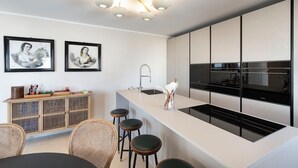 Eine moderne Küche mit einer zentralen Kochinsel, Barhocker, einem Esstisch und zwei gerahmten Kunstwerken an der Wand.