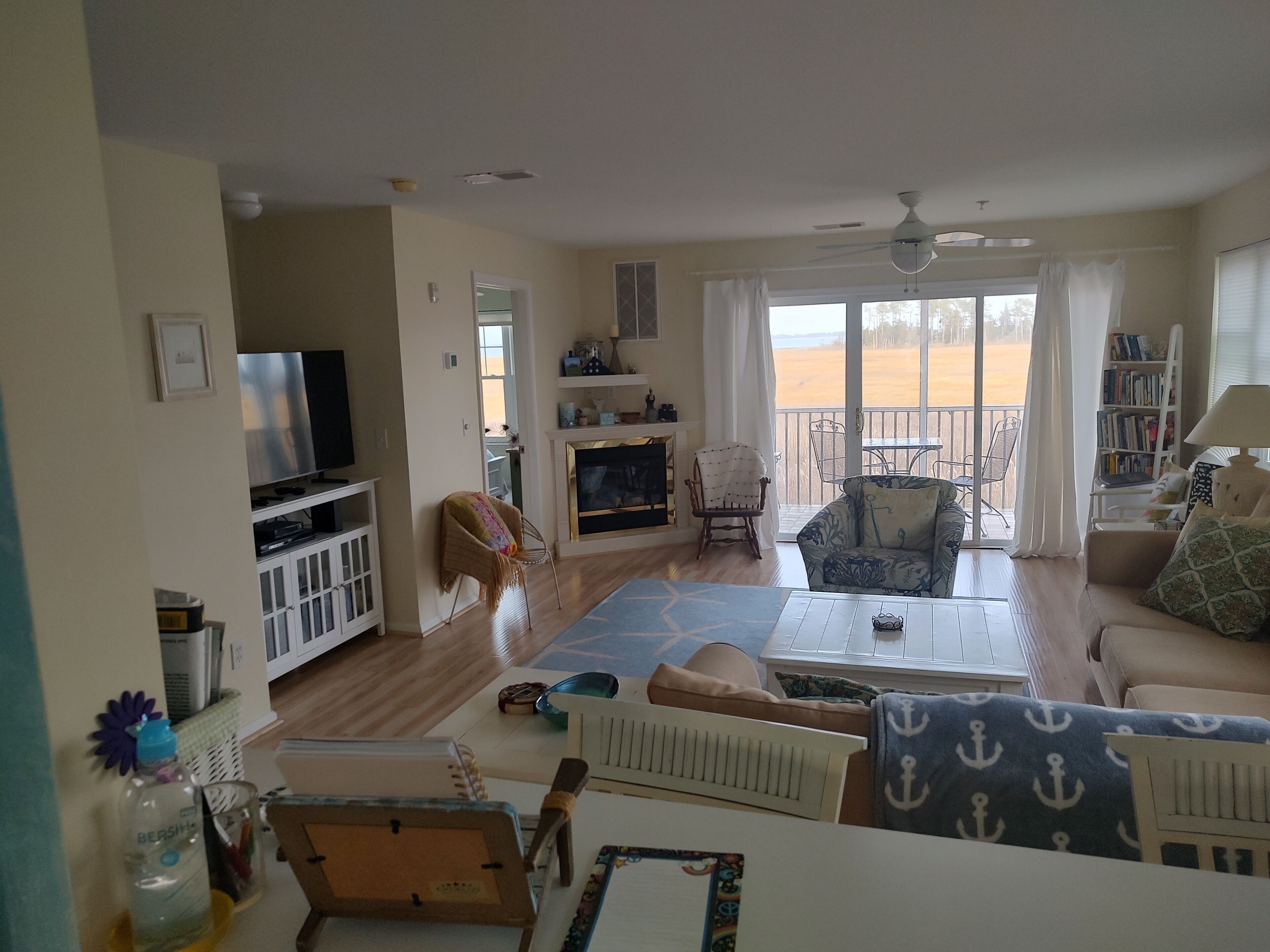 A spacious living room with a television, seating area, and a view of the beach through large windows.