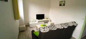 A small living area with a sofa, a television, a white cabinet, and a small table with a green object on it.