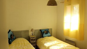 Een kamer met twee bedden, een nachtkastje met een lamp en een raam met gordijnen.