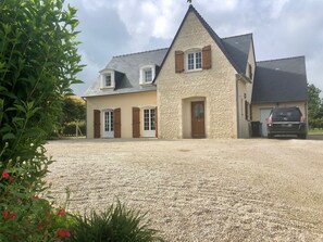 A two-story house with a stone facade, a gravel driveway, and a parked car.
