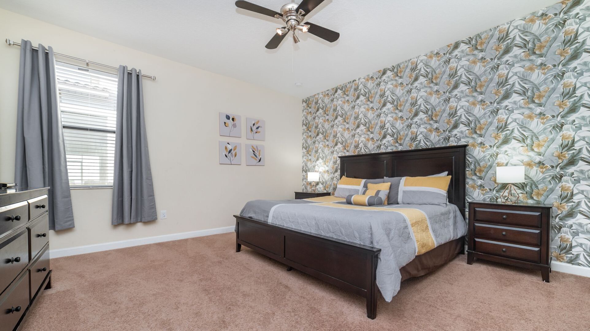 A bedroom with a bed, a nightstand, a dresser, a ceiling fan, and a window with curtains.