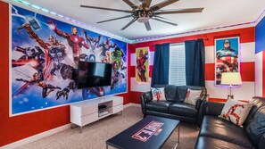 A living room with a large TV, a ceiling fan, and a red and blue wall mural.