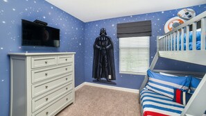 A room with a starry wall mural, a Darth Vader statue, a bunk bed with a Star Wars-themed bedspread, and a white dresser.